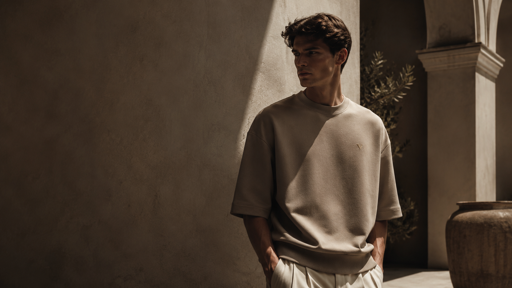 A man wearing a minimal ivory VARCHAX t-shirt in an architectural setting